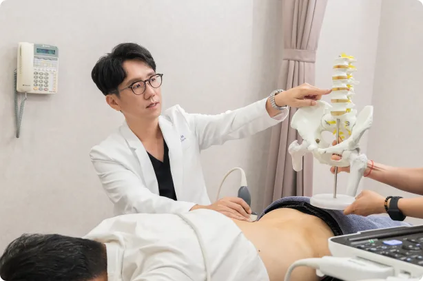蕙林診所醫師一手持超音波探頭、一手指著脊椎模型，向躺臥的患者解說