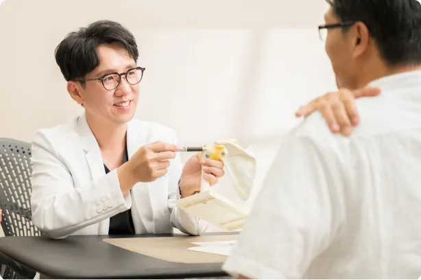 蕙林診所醫師手持肩關節模型，向坐在對面的患者說明