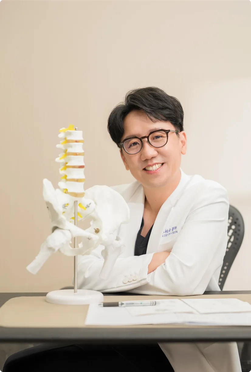 蕙林診所醫師微笑倚在診桌旁，桌上立著脊椎與骨盆模型